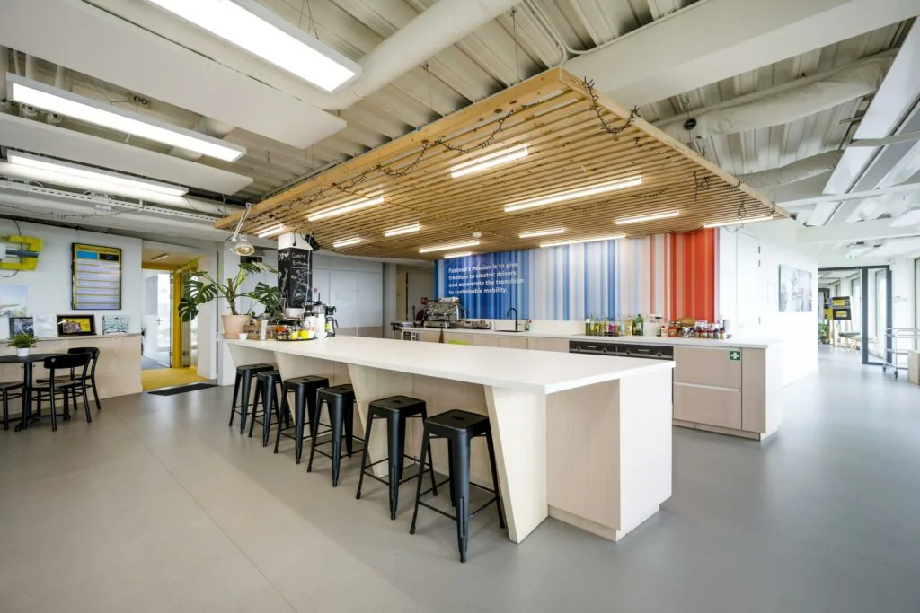 Moderne kantoorkeuken in de James Wattstraat met een lang wit kookeiland, barkrukken en kleurrijke wand met missiequote.